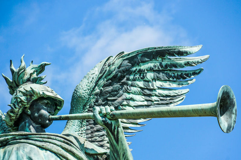 Low angle view of angel statue playing trumpet against blue sky