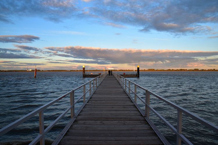 Pier leading to calm sea at sunset