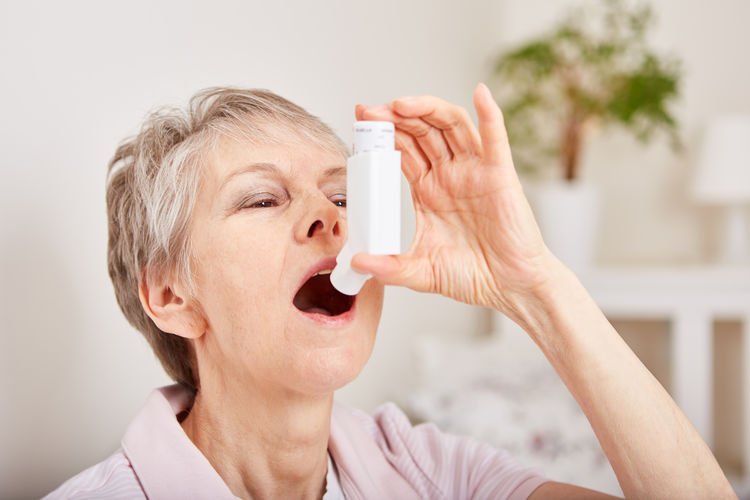 Senior woman applying asthma inhaler at home