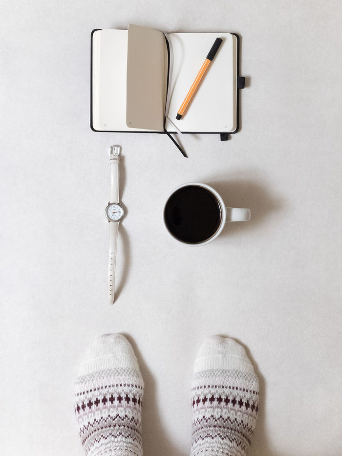 Low section of person standing by black coffee and diary with pen on white background