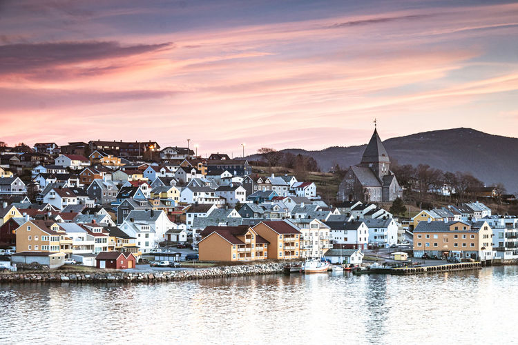 Townscape by lake against sky during sunset