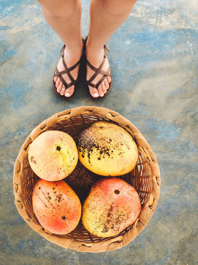 Low section of woman standing on mangoes in wicker basket at beach