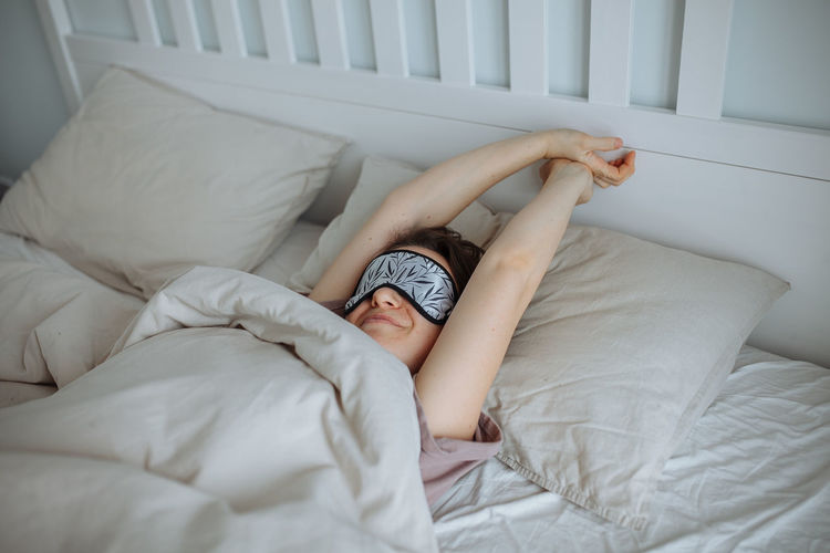 Happy young girl stretching in bed in the morning