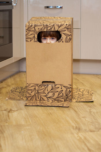 Portrait of a cute, blue-eyed baby girl playing with a cardboard box and hiding inside it