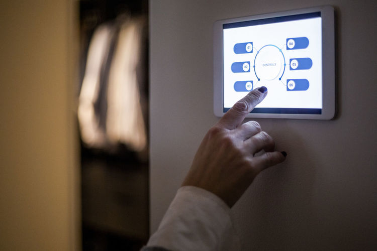 Cropped hand of woman using digital tablet mounted on wall at home
