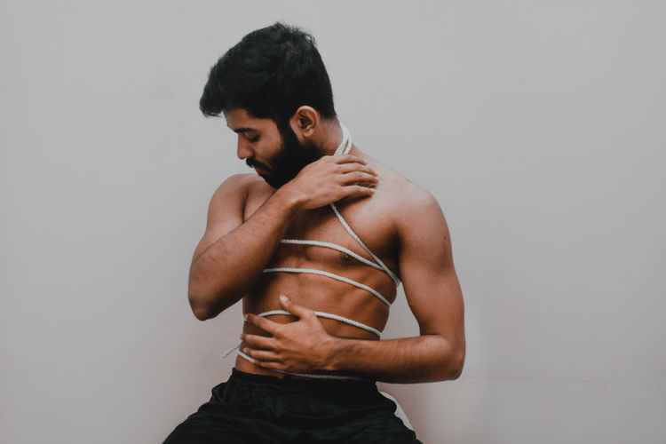 Full length of shirtless man standing against wall