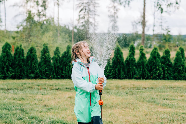 Girl spraying water in her face with a hose in the yard in summer