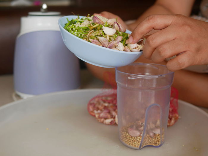 A woman's hands preparing / putting food ingredients in a blender cup for cooking food at home