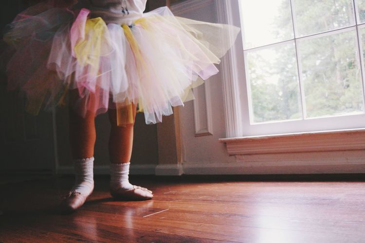 Low section of ballerina standing on hardwood floor at home