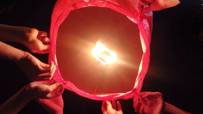 Cropped hands of friends holding illuminated paper lantern at night