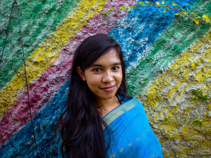 Portrait of smiling teenage girl standing by wall outdoors