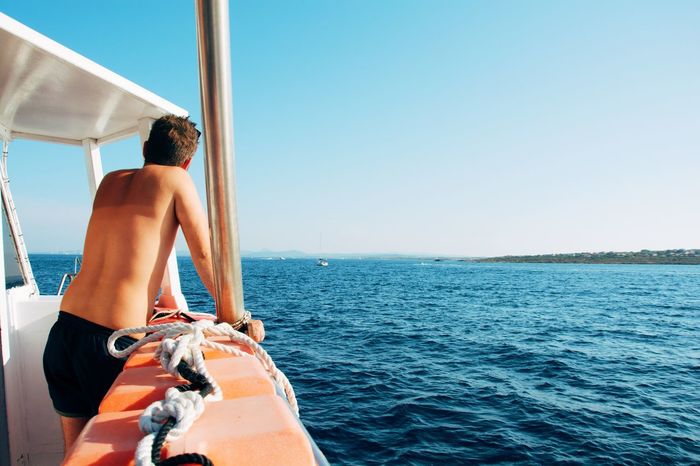 Rear view of shirtless man in boat against sky