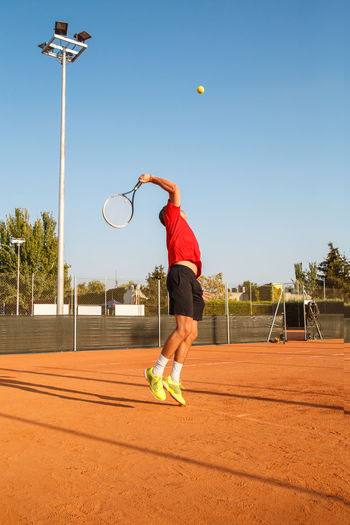 Man playing tennis on court against clear blue sky
