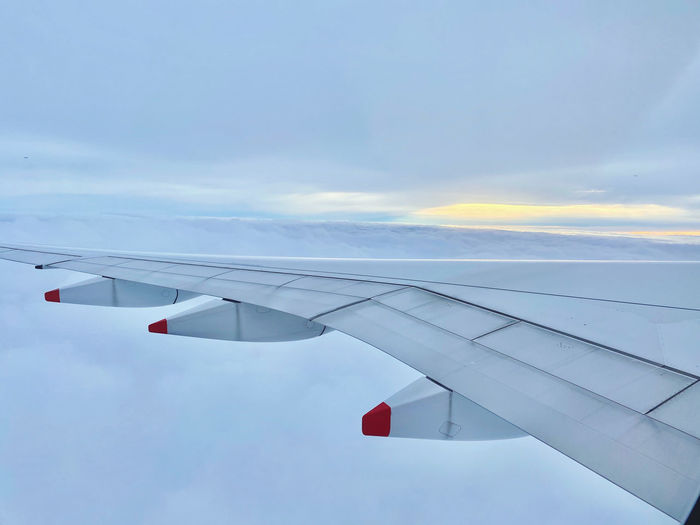 Landscape view of airplane wing surrounded by clouds and sunset in the distance 
