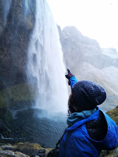 Woman pointing at waterfall against mountain