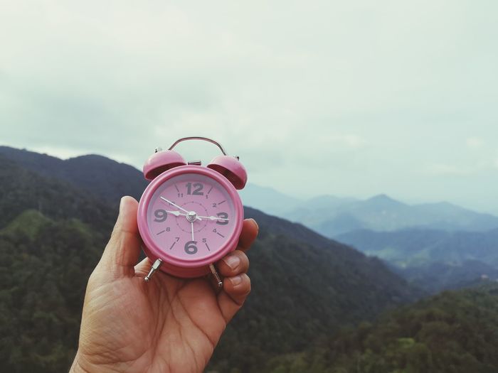 Cropped hand holding alarm clock against mountains