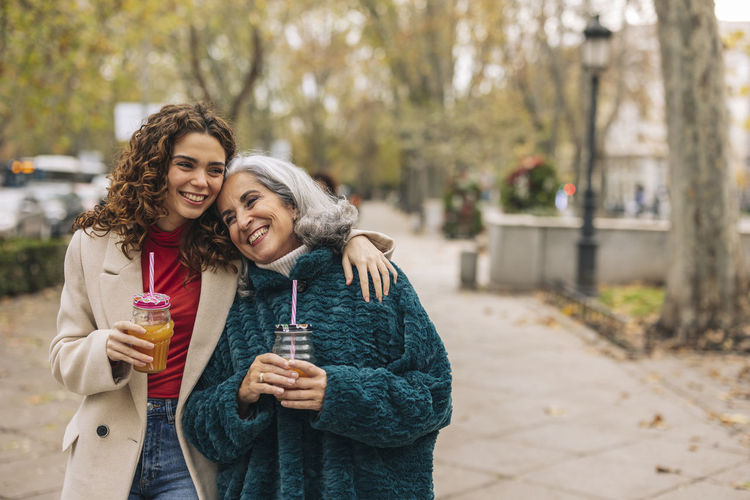 Happy young woman arm around with grandmother at footpath