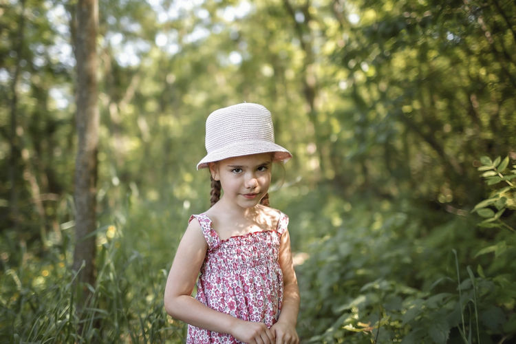 Portrait of cute girl wearing hat standing against trees