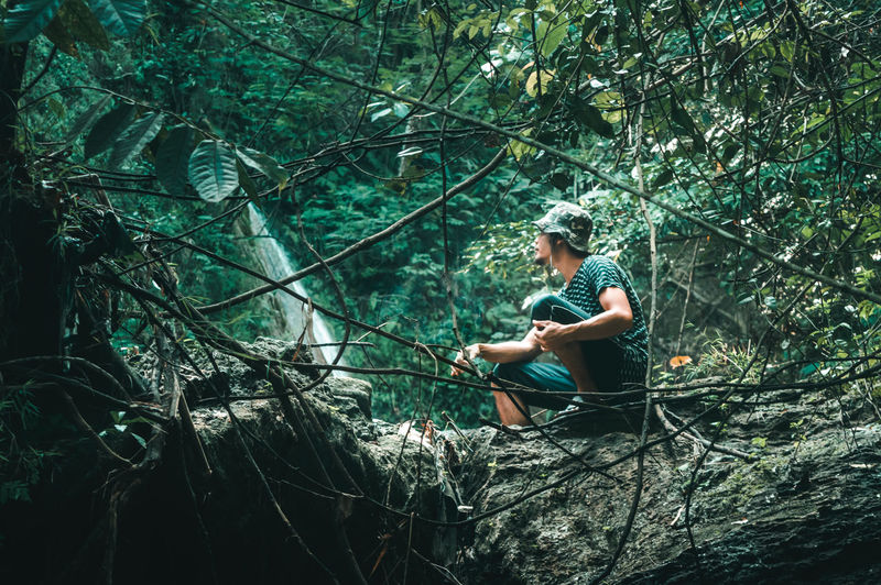 Low angle view of young man sitting on rock in forest