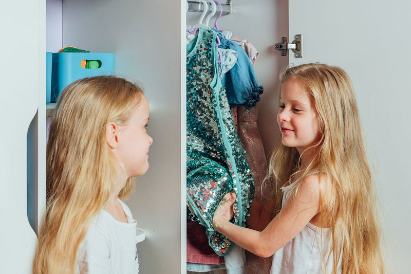Two little beautiful girls friends sisters play fashion, choose outfits, clothes from a white