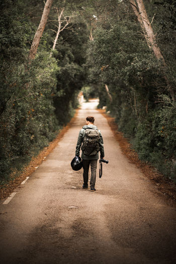 Man walking with helmet and camera on a road where trees make a tunnel