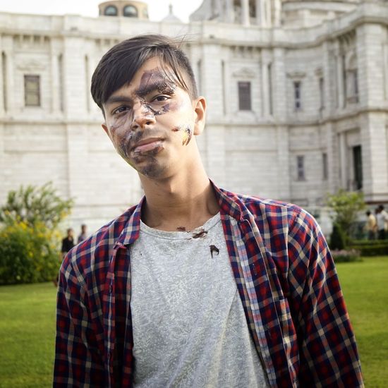Portrait of young man with messy face standing against building