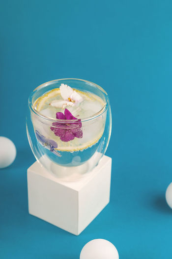 A glass of ice water decorated with edible violet flowers in a modern style among geometric shapes