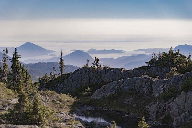 Hiker riding bicycle on mountain against sky