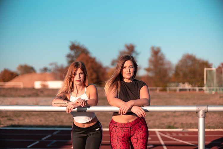 Portrait of young women standing at running track against sky