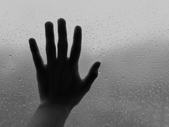 Human hand touching wet glass window