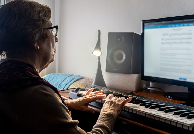 Caucasian elderly woman learning music and playing the musical keyboard.