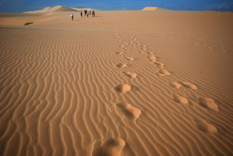 Distance shot of people walking at desert with footprints in foreground