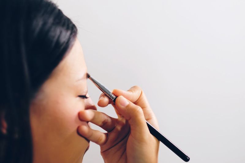 Close-up of woman applying make-up against white background