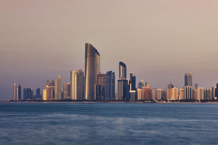 Sea by modern buildings in city against sky