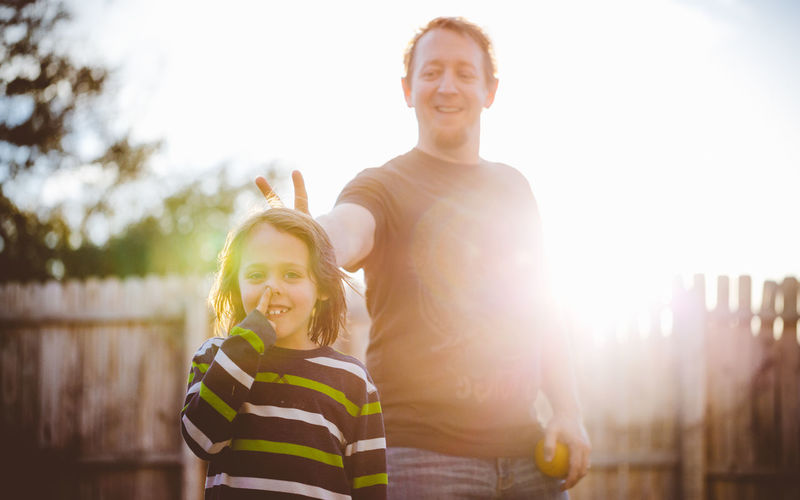 Smiling father making peace sign behind son in yard on sunny day