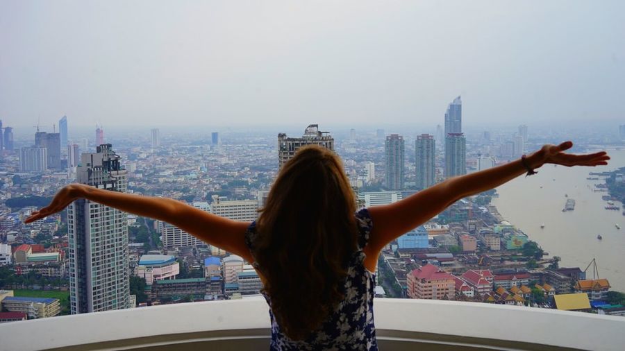 Rear view of woman standing in front of cityscape against sky