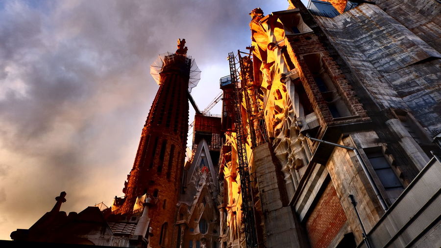 Low angle view of sagrada familia against cloudy sky during sunset