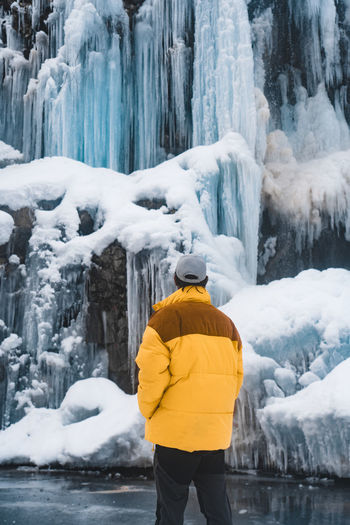 Rear view of man standing against frozen waterfall