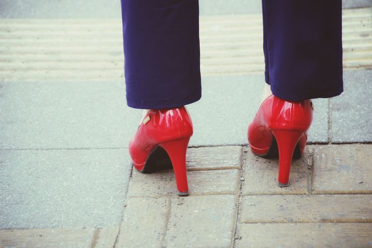 Low section of woman standing on footpath with red heels