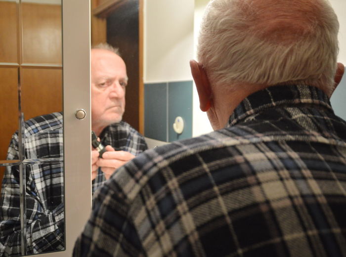 Reflection of man shaving on mirror in bathroom at home