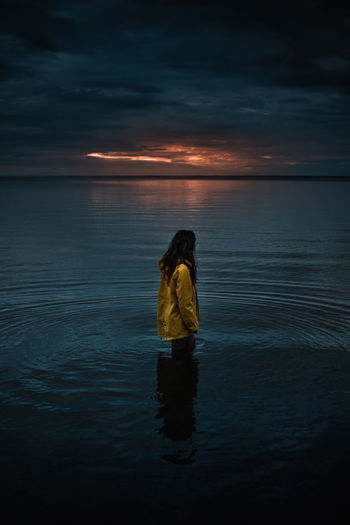 Woman standing on sea against sky during sunset