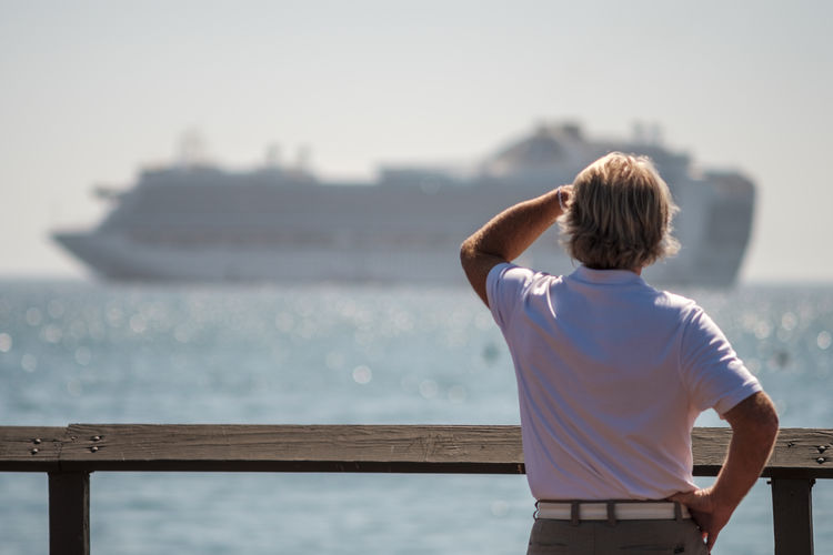 Rear view of man looking at ship sailing on sea against sky