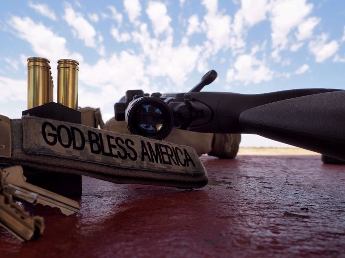 Close-up of text by gun and bullets against cloudy sky
