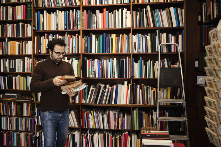 Customer choosing book while standing against bookshelves