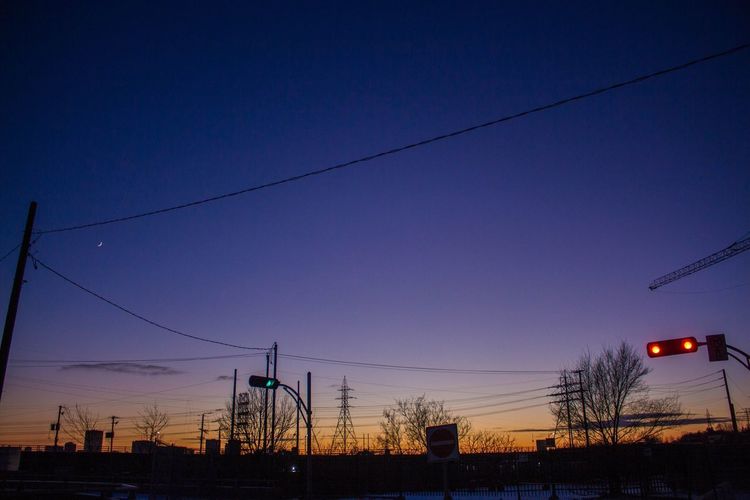 Low angle view of electricity pylons against sky at sunset