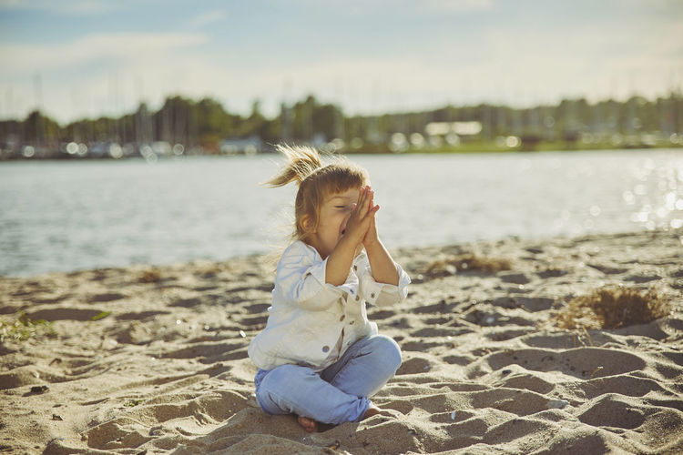 Charming child doing yoga on the beach
