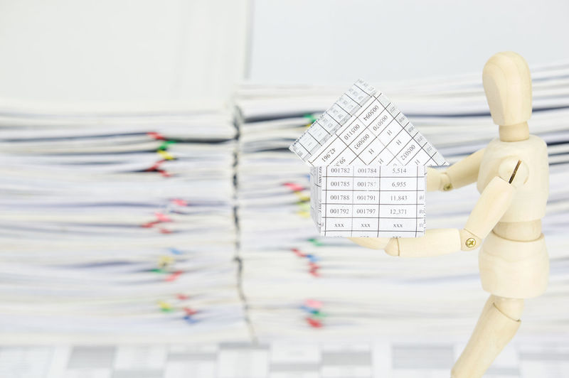 Close-up of wooden figurine holding model house against stacked files