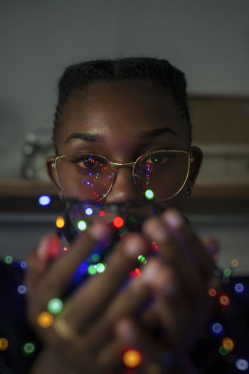 Close-up portrait of young adult wearing sunglasses holding christmas lights 