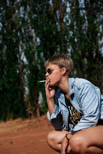 Woman smoking while crouching in forest