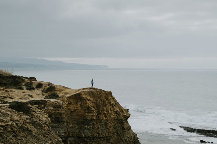 Mid distance view of man standing on cliff by sea